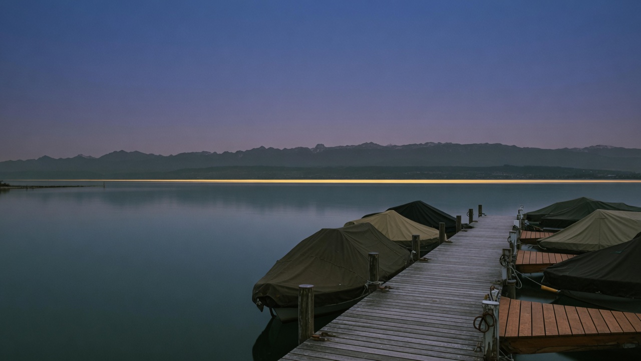 Abend am Bodensee: Steg, verdeckte Boote, goldene Linie am Horizont